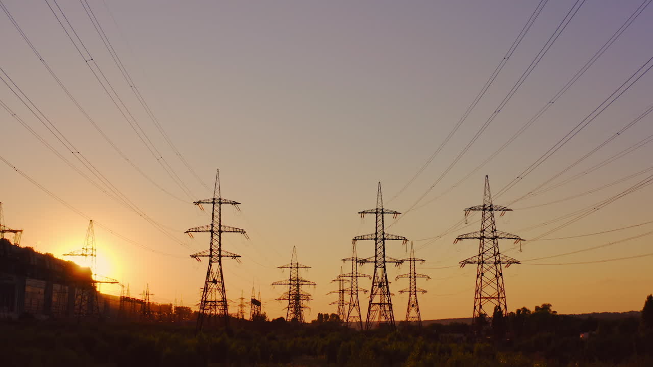 High-voltage electric line at sunset. Silhouettes of electric pylons on the setting sun background. Electricity distribution station.