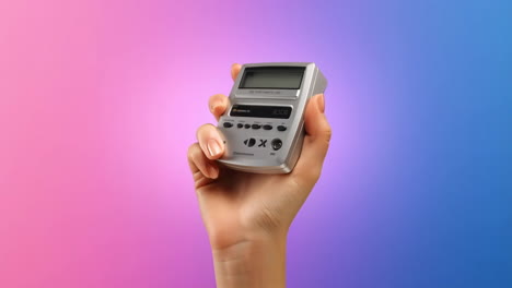 hand holding a small electronic device against a pink and blue gradient background