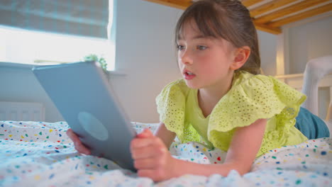 girl in bedroom at home lying on bed using digital tablet