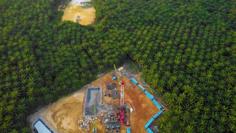 cinematic 4k drone footage of onshore drilling rig equipment structure for oil exploration and exploitation in the middle of jungle surrounded by palm oil trees during sunset and high oil price