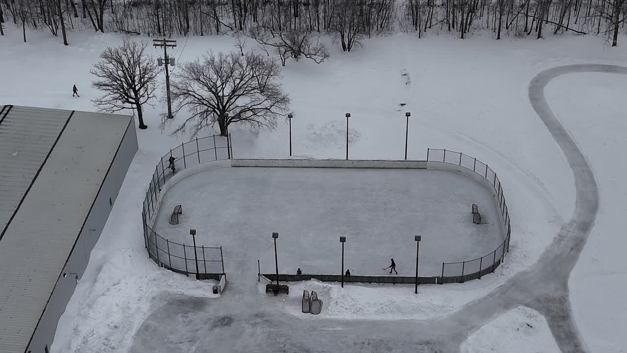 Letecký dron přibližuje a obíhá doprava kolem venkovního kluziště ve Winnipegu, Manitoba, Kanada. Děti hrají hokej na sněhem pokrytém ledu s blízkými domy a komunitním centrem.