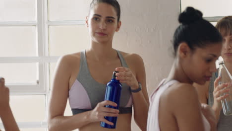 group of healthy young women in yoga class drinking water resting after intense training workout in fitness studio