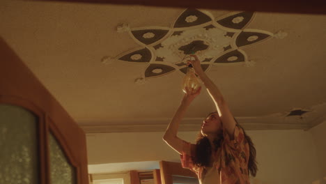 joven instalando una bombilla bajo el techo adornado en una habitación bien iluminada