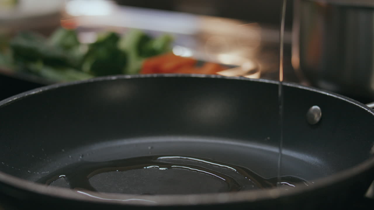 Nærbillede af hældning af madolie i stegepande i restaurantkøkken.