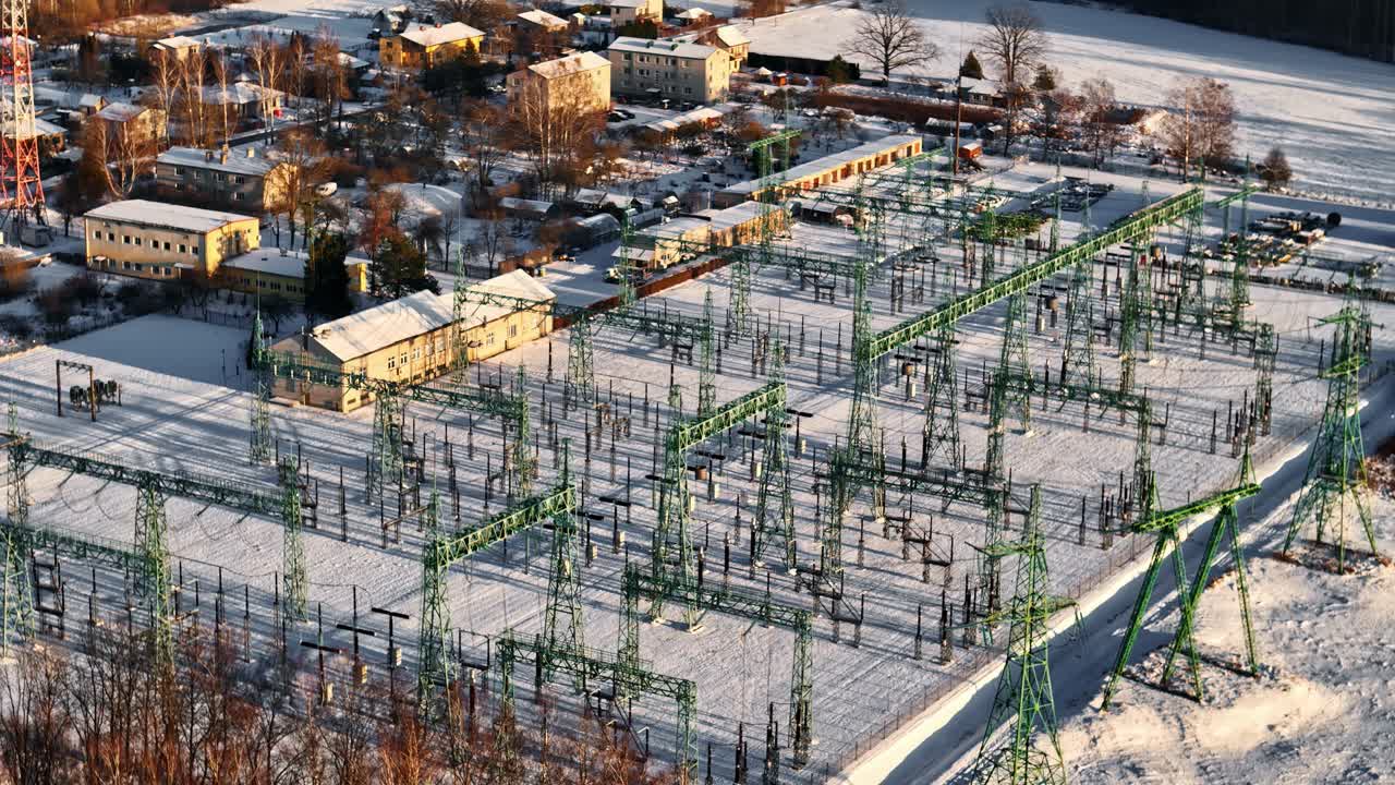 Snow covered electrical substation with steel lattice structures and power lines in winter sunlight
