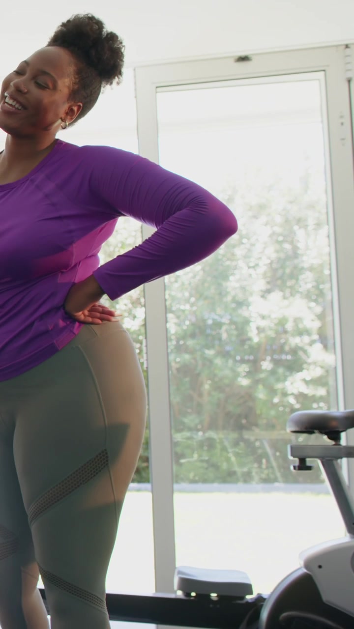 Mid-adult woman finishing workout cooling down, stretching back and checking form near glass doors