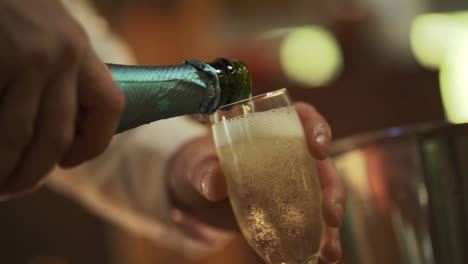 las manos del hombre sosteniendo una botella verde vertiendo champán en un vaso para la celebración