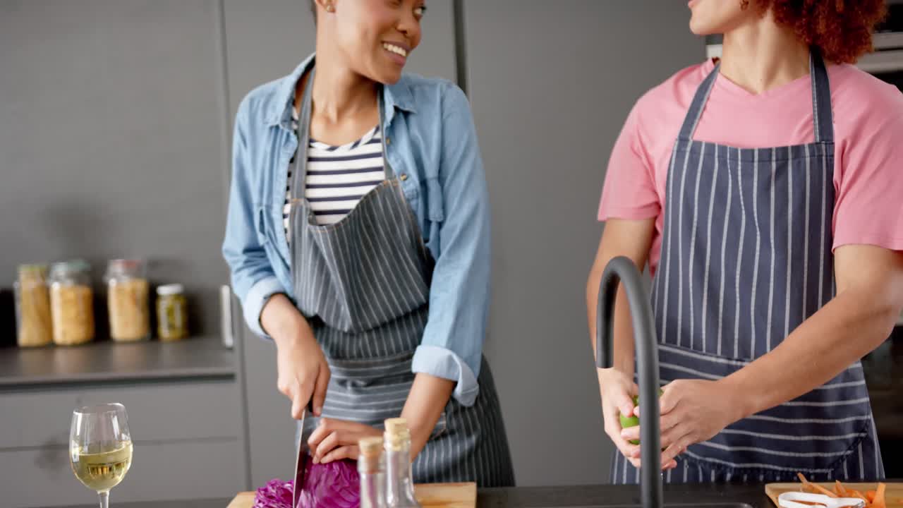 pareja feliz diversa en delantales preparando verduras juntos y hablando en la cocina, cámara lenta
