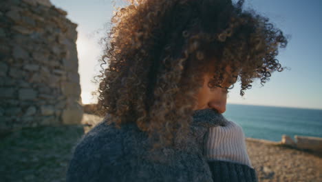 curly lady standing sea beach feeling cold adjusting coat closeup. woman warming