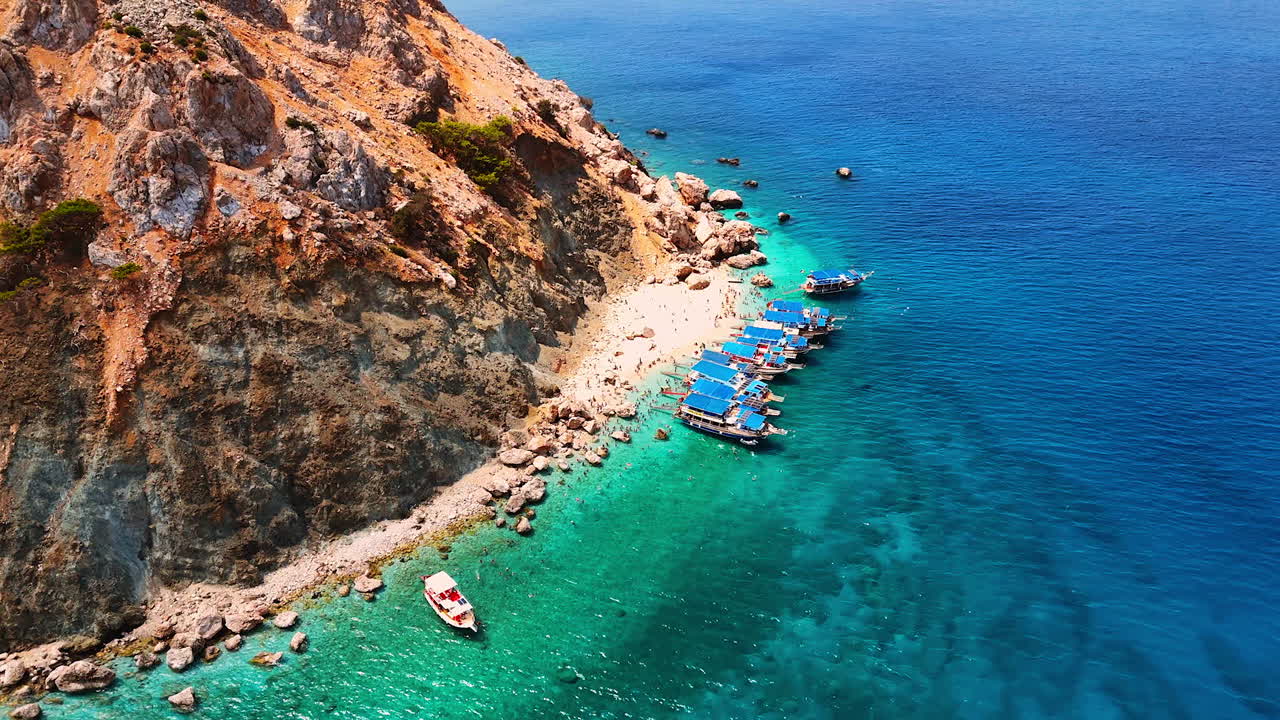 Boats by rocky shore view. Boats are anchored by a rocky coastline under a clear blue sky near the water's edge on a sunny day