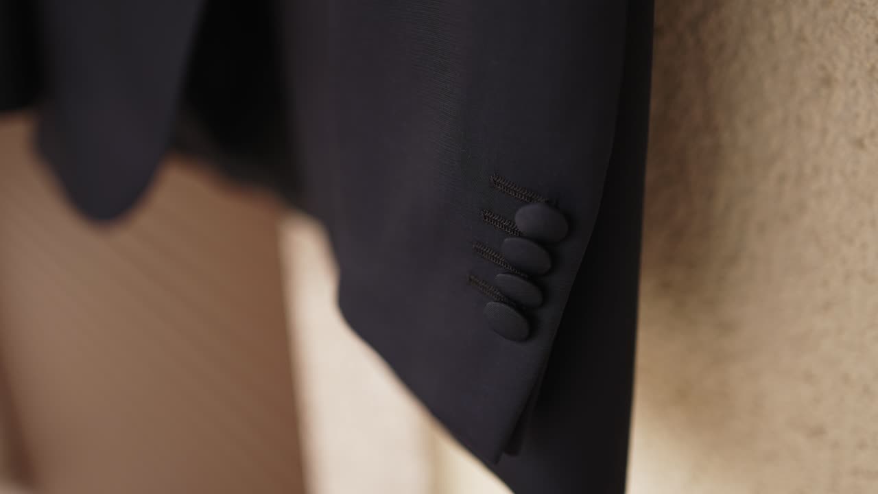 Close up of a dark suit sleeve showing four fabric covered buttons