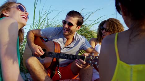 amigos étnicos tocando la guitarra en un picnic en la playa
