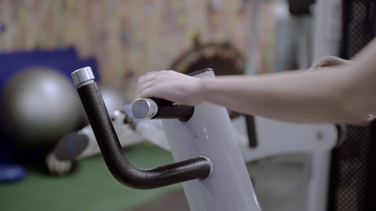 Woman hand sanitising the handles of a gym equipment with alcohol spray. Reopening precautions for the COVID pandemic.