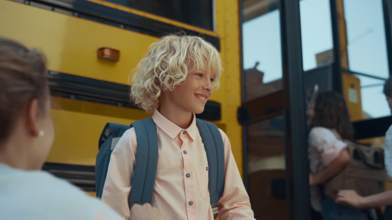 Skole dreng giver en high five til omsorgsfuld mor, nærbillede. Forskellige elever stiger på skolebussen.