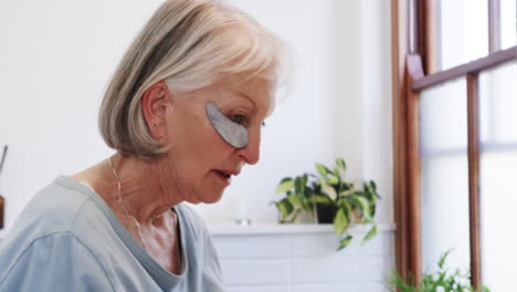 senior woman applying eye patches at home, focusing on self-care routine