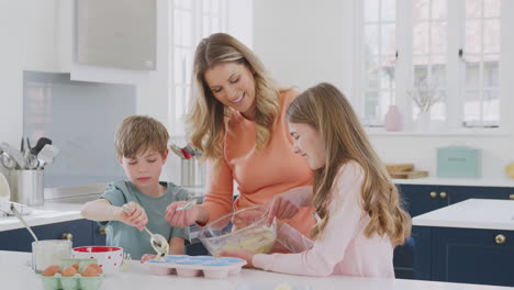 mother with two children in kitchen at home having fun baking cakes together