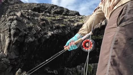 primer plano de una persona pescando con mosca, carrete en foco con telón de fondo rocoso, actividad de ocio al aire libre