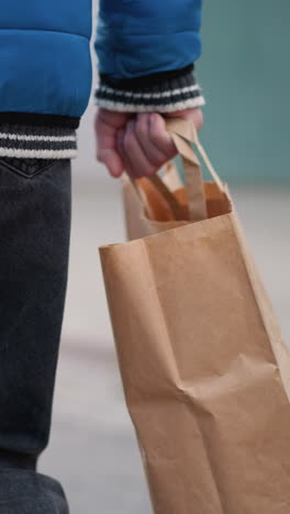 vista trasera del brazo y el lado del individuo en una chaqueta azul brillante sosteniendo una bolsa de compras, ambientada contra un fondo urbano borroso, destacando la vida cotidiana casual