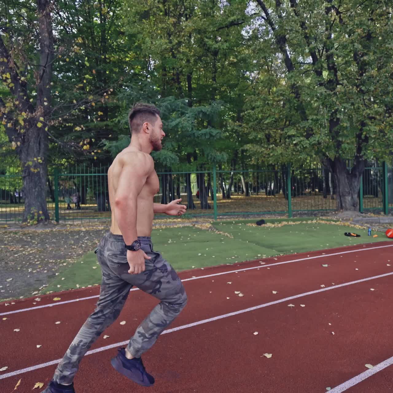 Male sprinter training for race. Back view of athlete without shirt starting running at outdoor athletics track and field stadium. Sport and fitness concept.