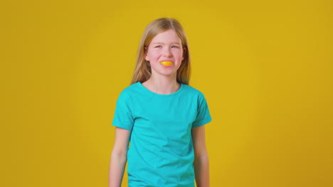 studio portrait of girl using orange segment for mouth and teeth against yellow background