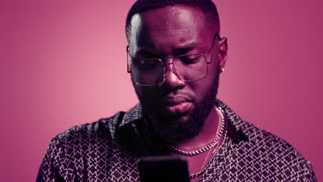 hombre afro leyendo un mensaje en el estudio. hombre usando un teléfono inteligente sobre un fondo rosa