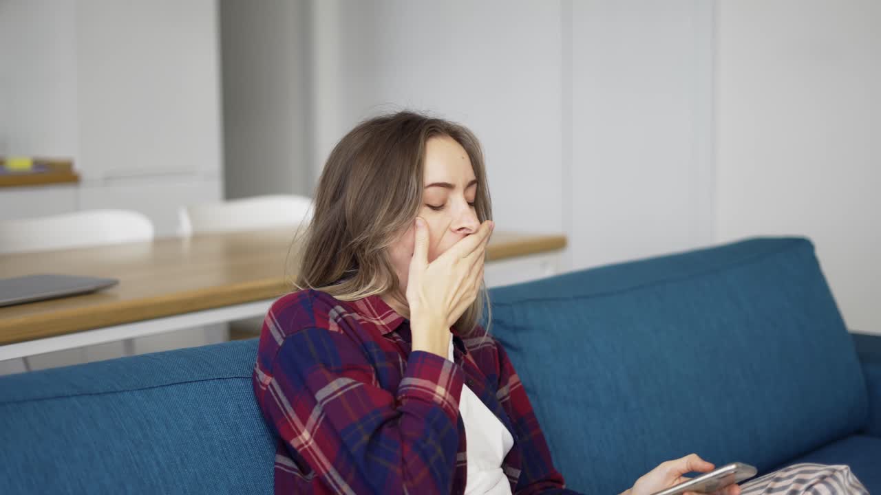 mujer aburrida chequeando teléfono inteligente sentada en un sofá en casa