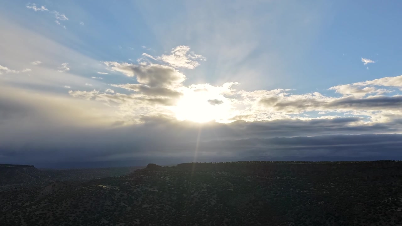 4K drone timelapse features cinematic sun beams and shimmering light rays piercing dark storm clouds. Radiant crepuscular light shifts over a rugged high altitude mountain landscape at sunset.