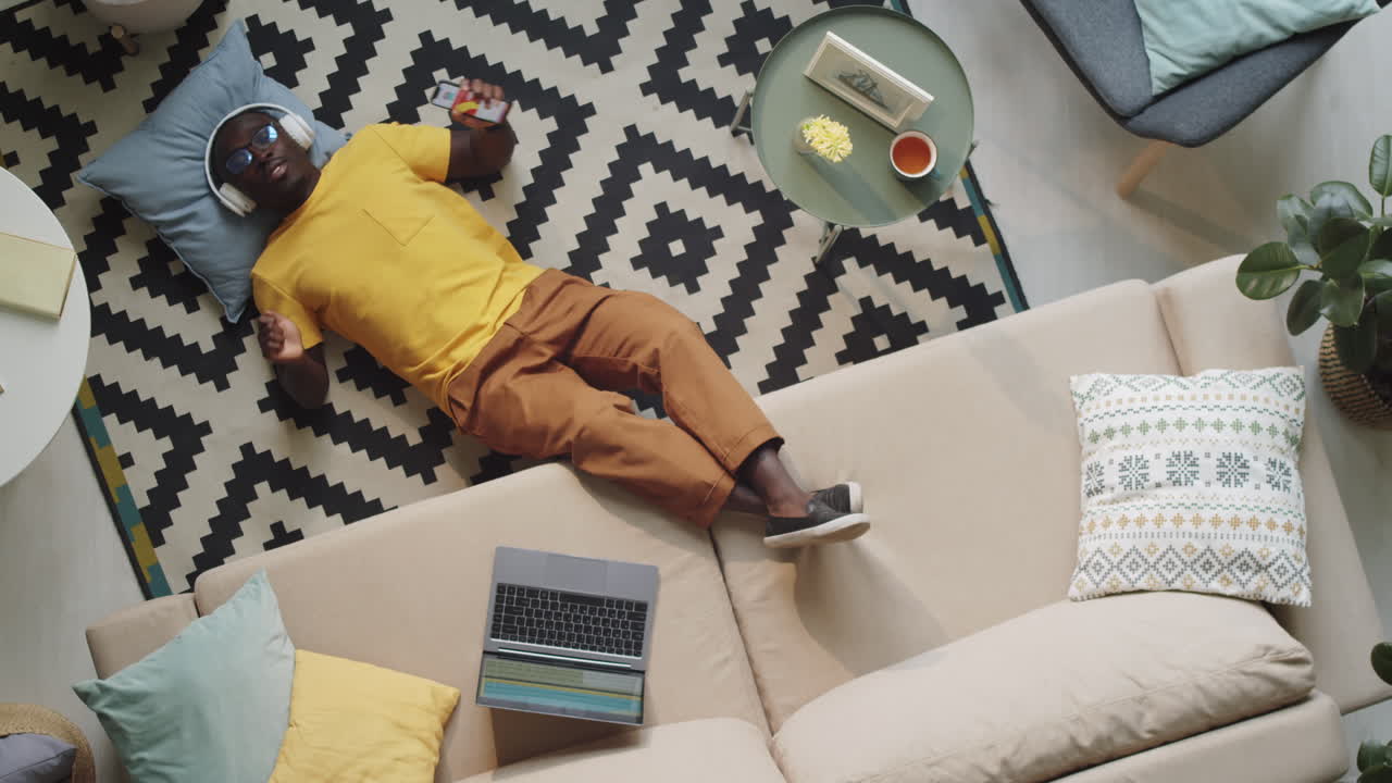hombre negro con auriculares disfrutando de la música mientras está acostado en el suelo