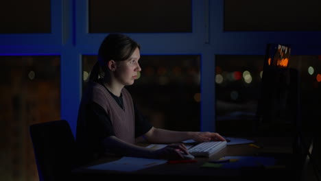 Young-good-looking-Caucasian-woman-typing-and-working-on-the-laptop-computer-as-freelancer-while-sitting-at-home-in-the-cozy-dark-living-room-with-a-cat.-At-night.-Stay-home