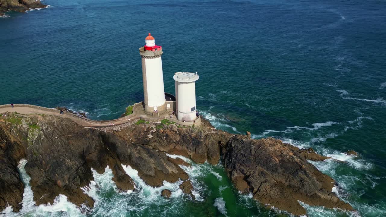 Aerial orbit of Petit Minou lighthouse on rocky coast with waves crashing and strong blue sea
