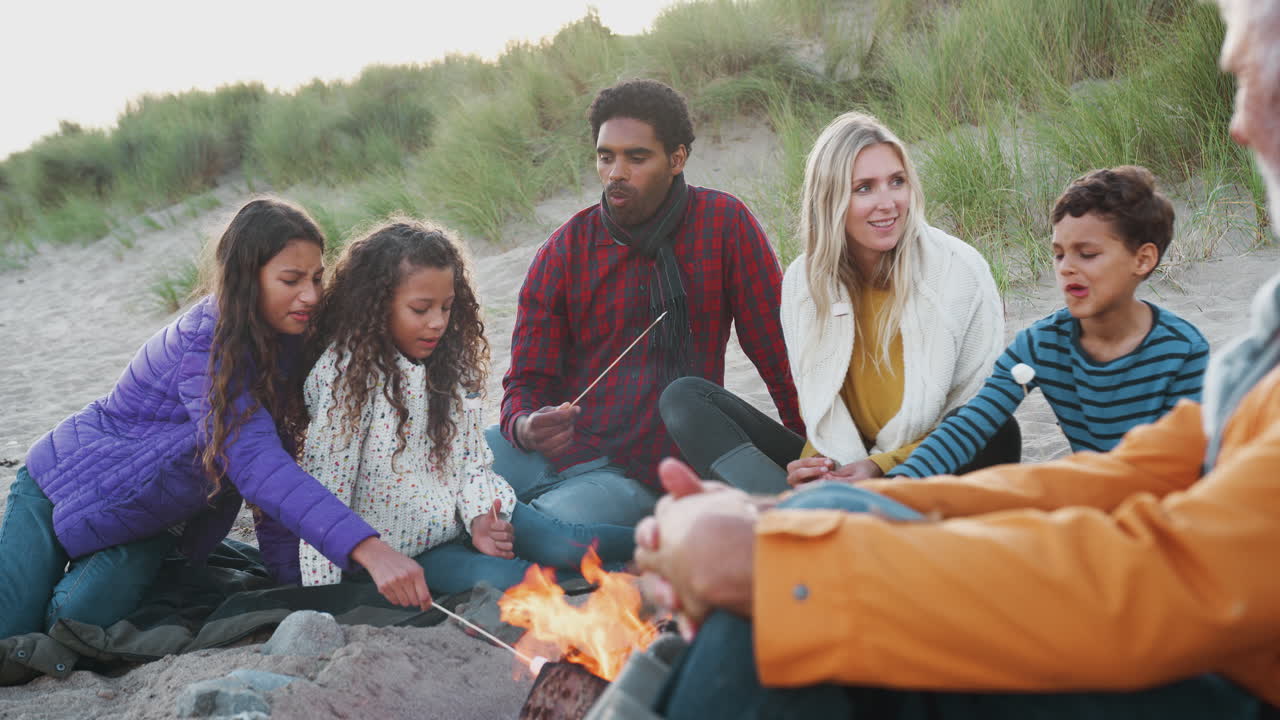 familia de varias generaciones tostando malvaviscos alrededor del fuego en vacaciones de playa de invierno