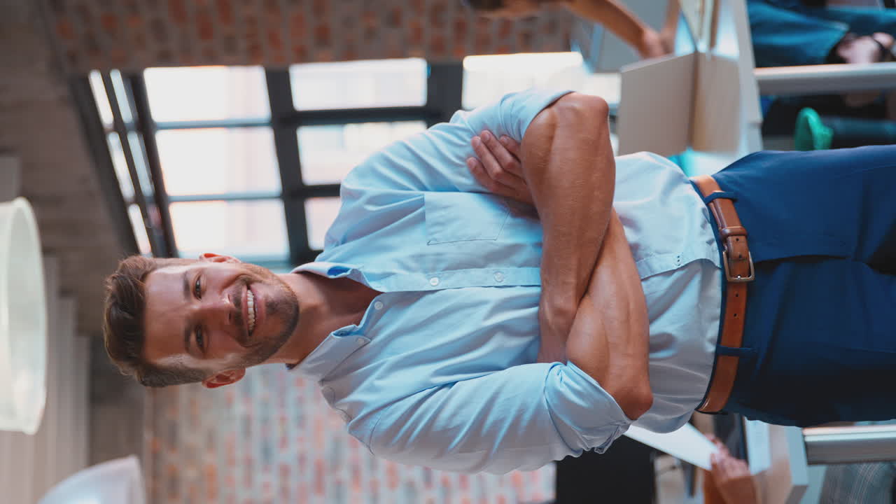 retrato de video vertical de un hombre de negocios sonriente en una oficina ocupada con colegas trabajando en el fondo