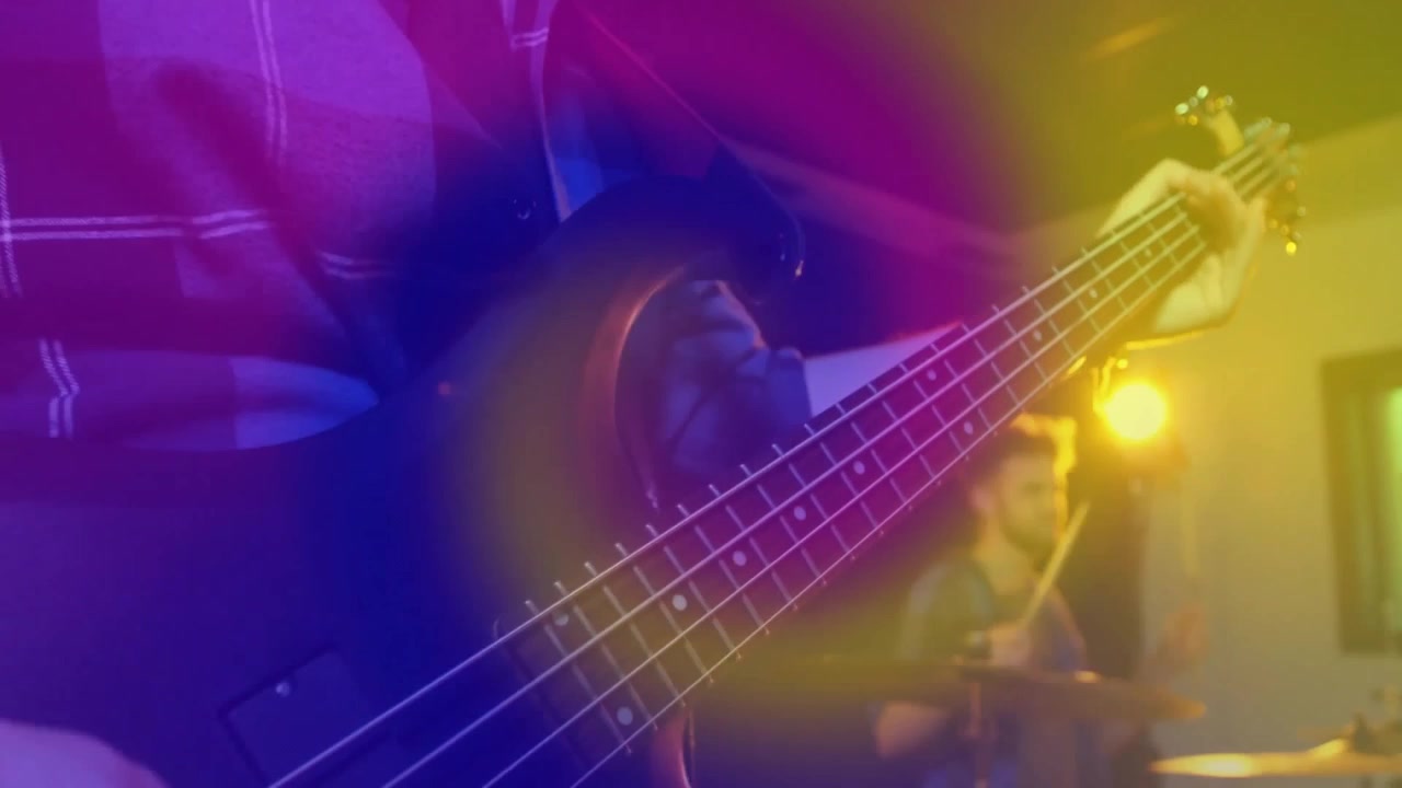 Bassista che pizzica una corda del basso, attivando anelli al neon e creando un groove musicale con il batterista.