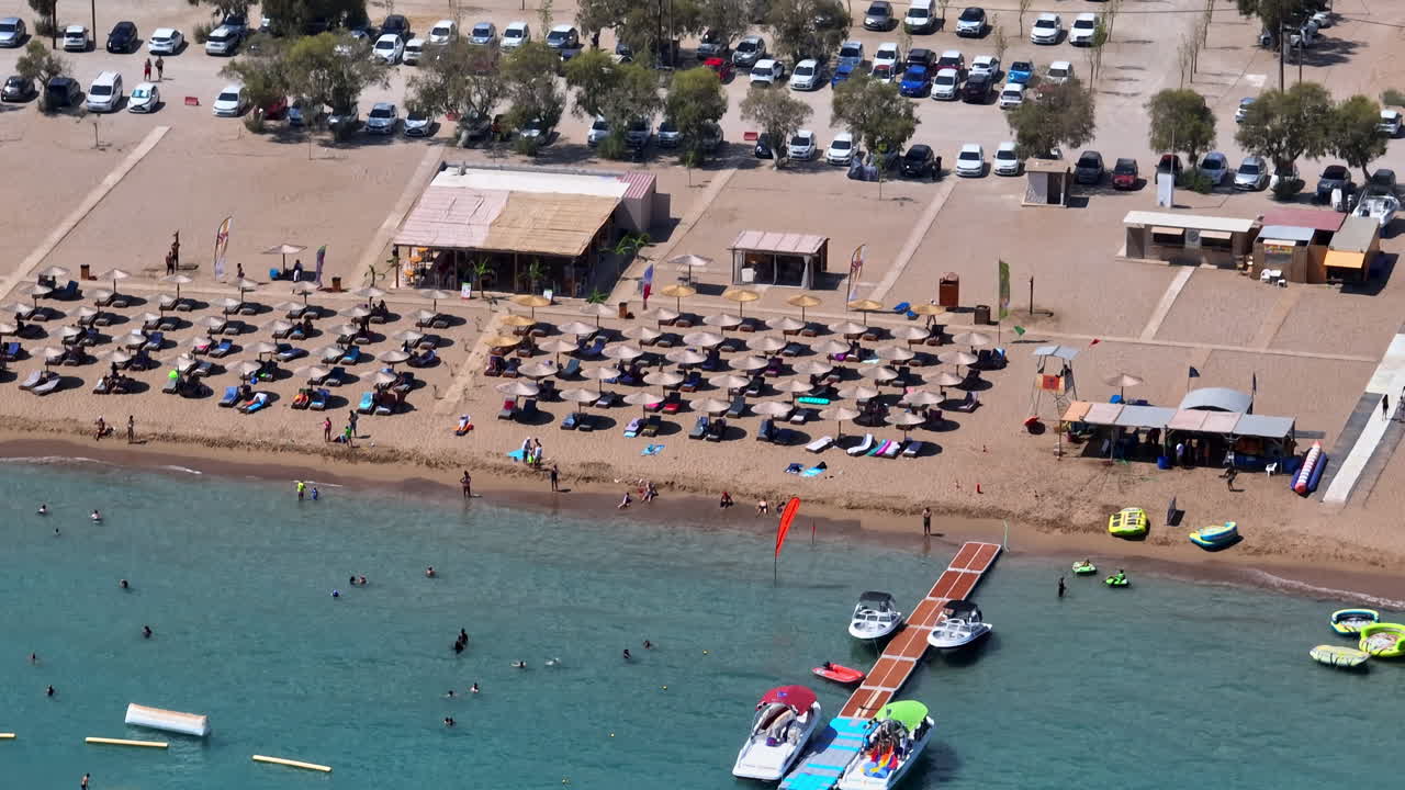 Aerial tracking shot of people and sunbeds at Faliraki beach, sunny day in Rhodes