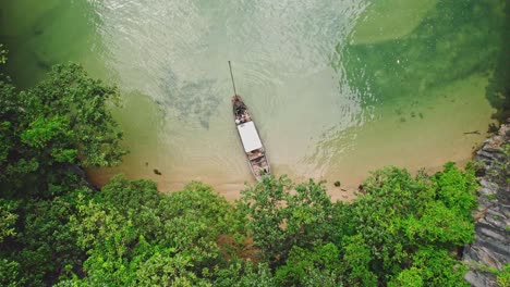 Captivating-Aerial-Perspective-of-a-Long-Tail-Boat-Overlooking-Turquoise-Waters-and-Limestone-Cliffs-at-Blue's-Hong,-Ko-Roi,-Thailand