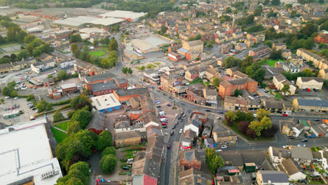 A-drone-records-Heckmondwike,-UK,-with-industrial-buildings,-bustling-streets,-and-the-old-town-center-on-a-summer-evening