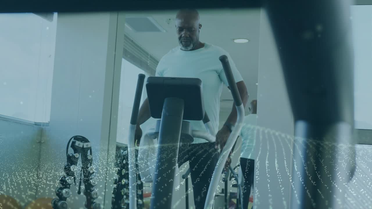 Mature man working out on elliptical in gym, sweating, wiping towel, checking console, resuming