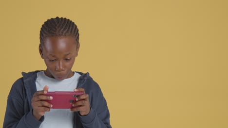 studio portrait of excited boy on asd spectrum gaming on mobile phone on yellow background