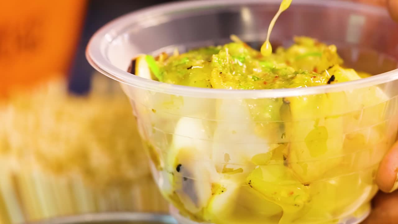 Close-up of squid salad being garnished with green sauce in a clear plastic cup.