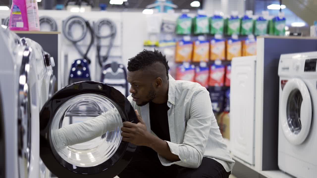 Black man is choosing washing machine in home appliances store, viewing exhibition sample