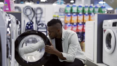 Black-man-is-choosing-washing-machine-in-home-appliances-store,-viewing-exhibition-sample