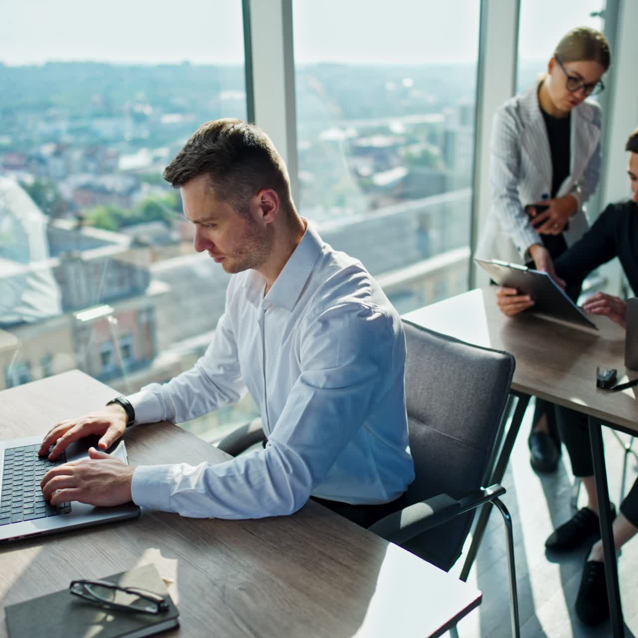 Team di giovani impiegati che lavorano in ufficio. Uomo in camicia bianca seduto alla reception che lavora al laptop. Un uomo in camicia nera dietro di lui parla con una collega in piedi accanto a lui e discutono di documenti.