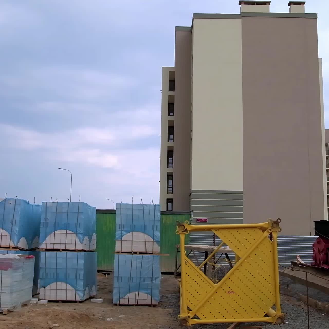 Lower part of crane on the rails near the piles of white bricks. Construction site outdoors. Newly built house at backdrop