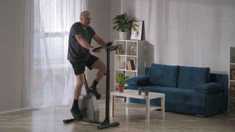 training on exercise bike for losing weight and keeping physical condition middle aged man is spinning pedals at home