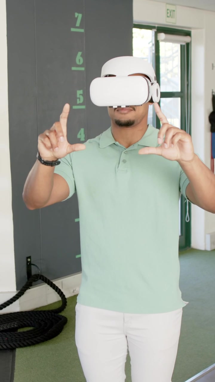 Video verticale: Uomo con visore VR in palestra, che fa gesti di pizzico per selezionare oggetti virtuali.