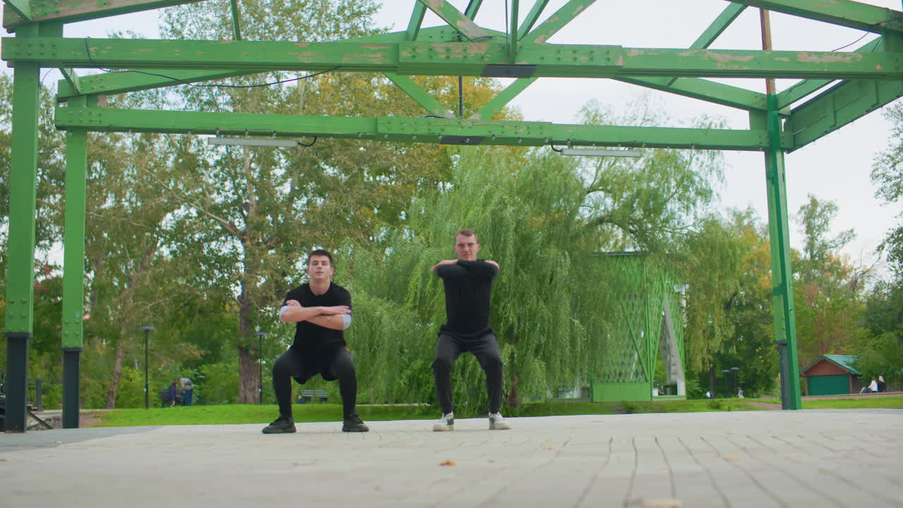 To hvide mænd laver en viral park-danse-udfordring under en grøn pergola med opløftende rytmer og armkoreografi, legende konkurrence mellem venner, træer ved søen og urbant baggrundsmiljø, filmet indhold