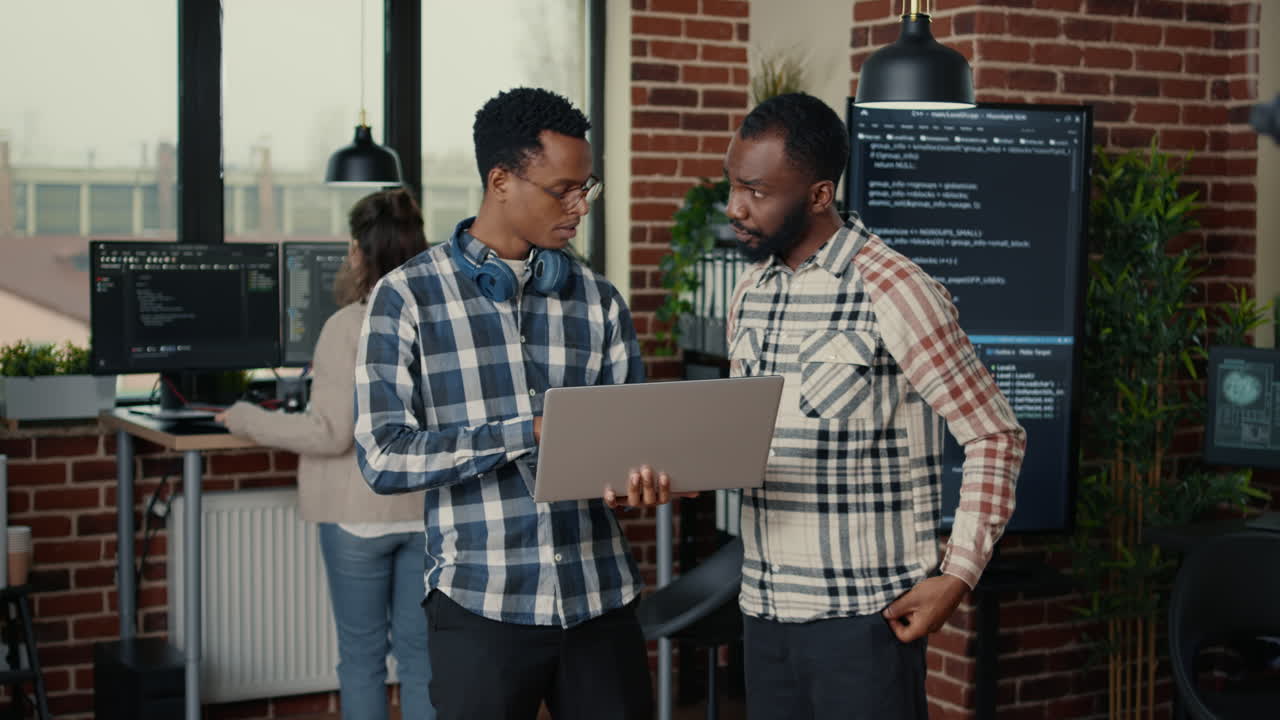 Software programmers talking about algorithms holding laptop and standing in the middle of it office