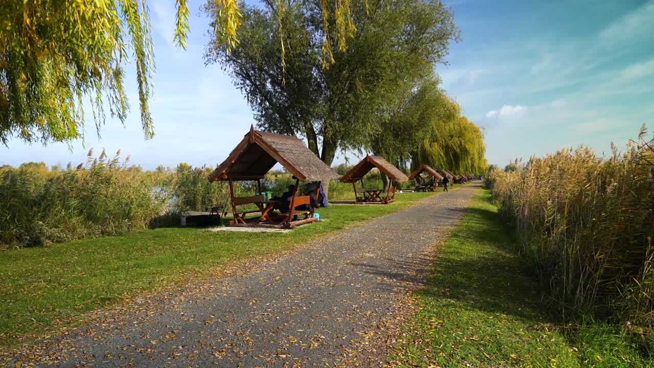 Outdoor wooden shelters along a lakeside path in Akasztó, Hungary under clear autumn skies