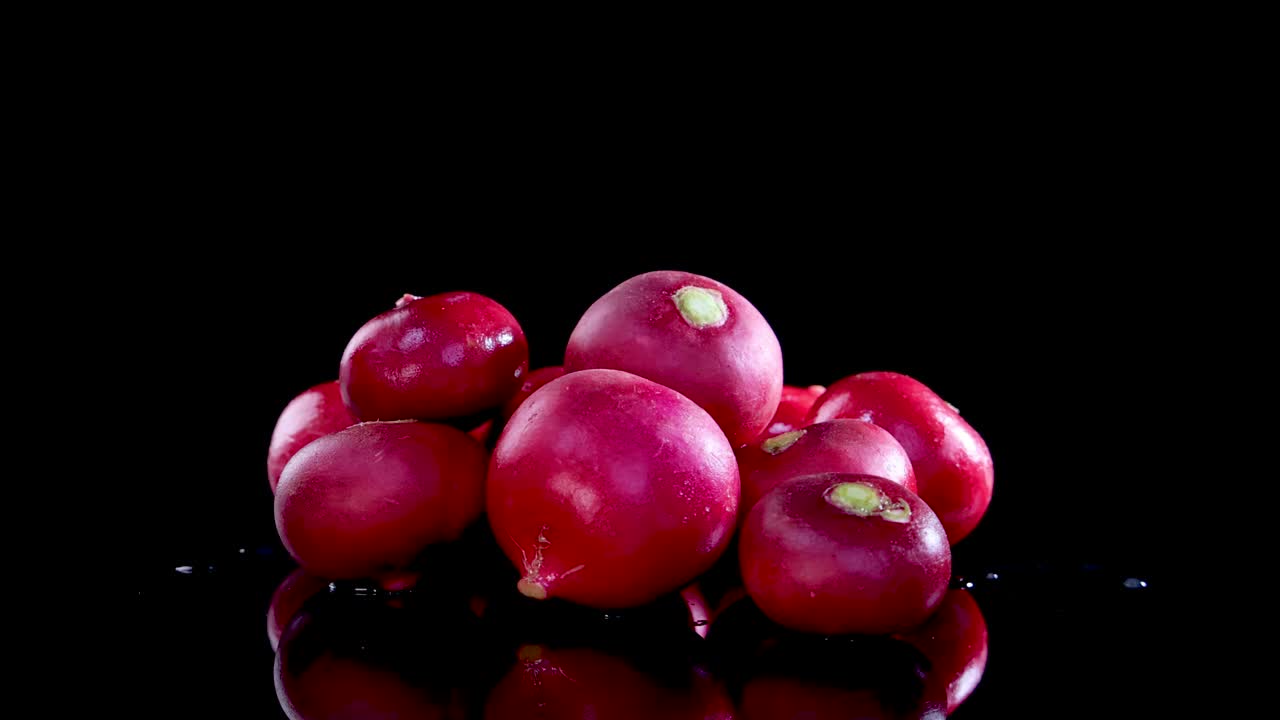 A pile of radishes rotates on a reflective surface under bright studio lighting, creating a dynamic visual effect