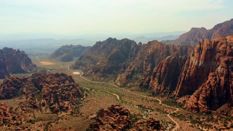 Aerial-drone-landscape-nature-trucking-right-shot-of-stunning-red-rock-formations-with-a-large-valley-and-dried-river-bed-below-on-a-hike-in-Snow-Canyon-State-Park,-Utah-on-a-warm-sunny-summer-day